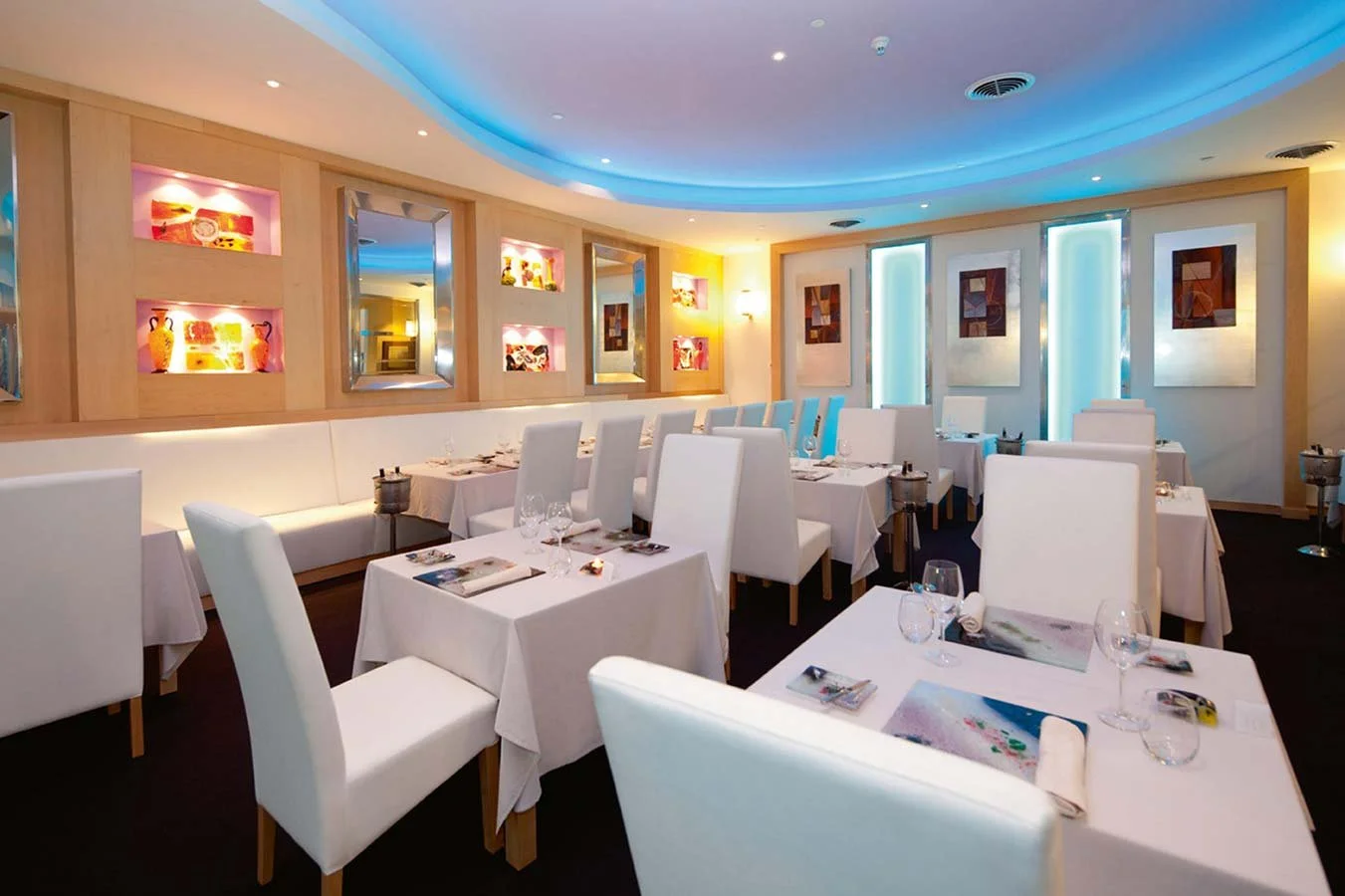 Elegant restaurant dining room with white tables and chairs, wall art, and soft lighting.
