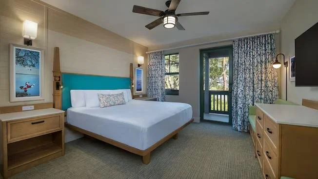 Hotel room with a king-sized bed, wooden furniture, a ceiling fan, and windows with blue curtains.