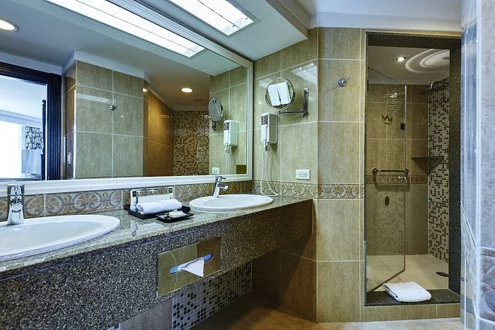 Bathroom with a double sink vanity, large mirror, shower area with clear door, and tiled walls.