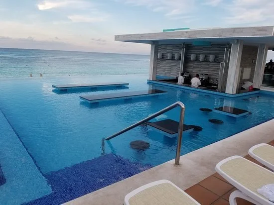 Poolside bar overlooking the ocean at sunset, with lounge chairs nearby.