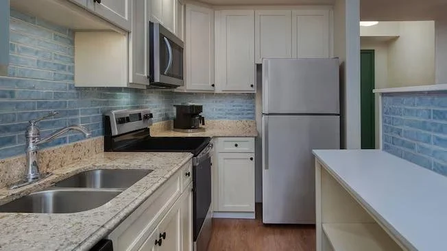 Kitchen with granite countertops, white cabinets, stainless steel appliances, including a refrigerator, stove, and microwave, with a blue brick backsplash.