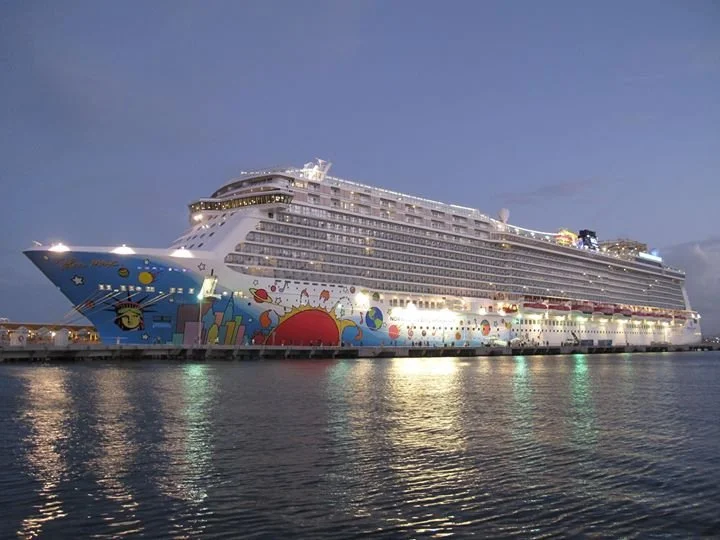 A large cruise ship docked at a port during the evening, with colorful artwork featuring a sun, playful shapes, and characters on its hull.