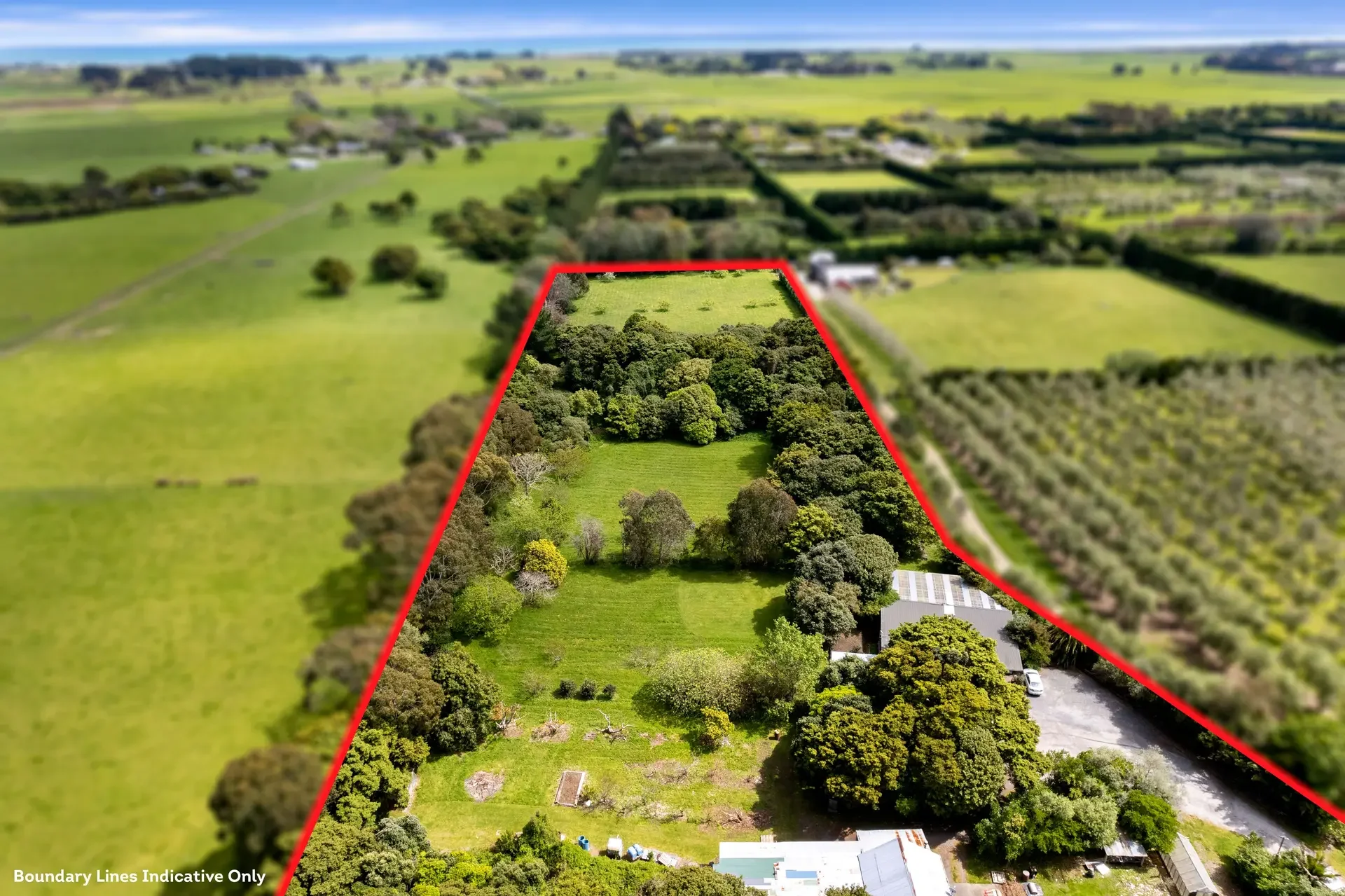Aerial view of a large rural property outlined with red boundary lines, featuring trees, open grassy areas, and buildings, surrounded by farmland and fields.