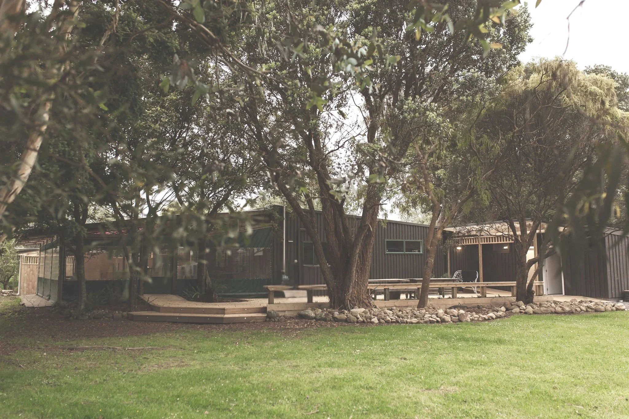 A modern black house with large windows, surrounded by tall trees and a well-maintained lawn.