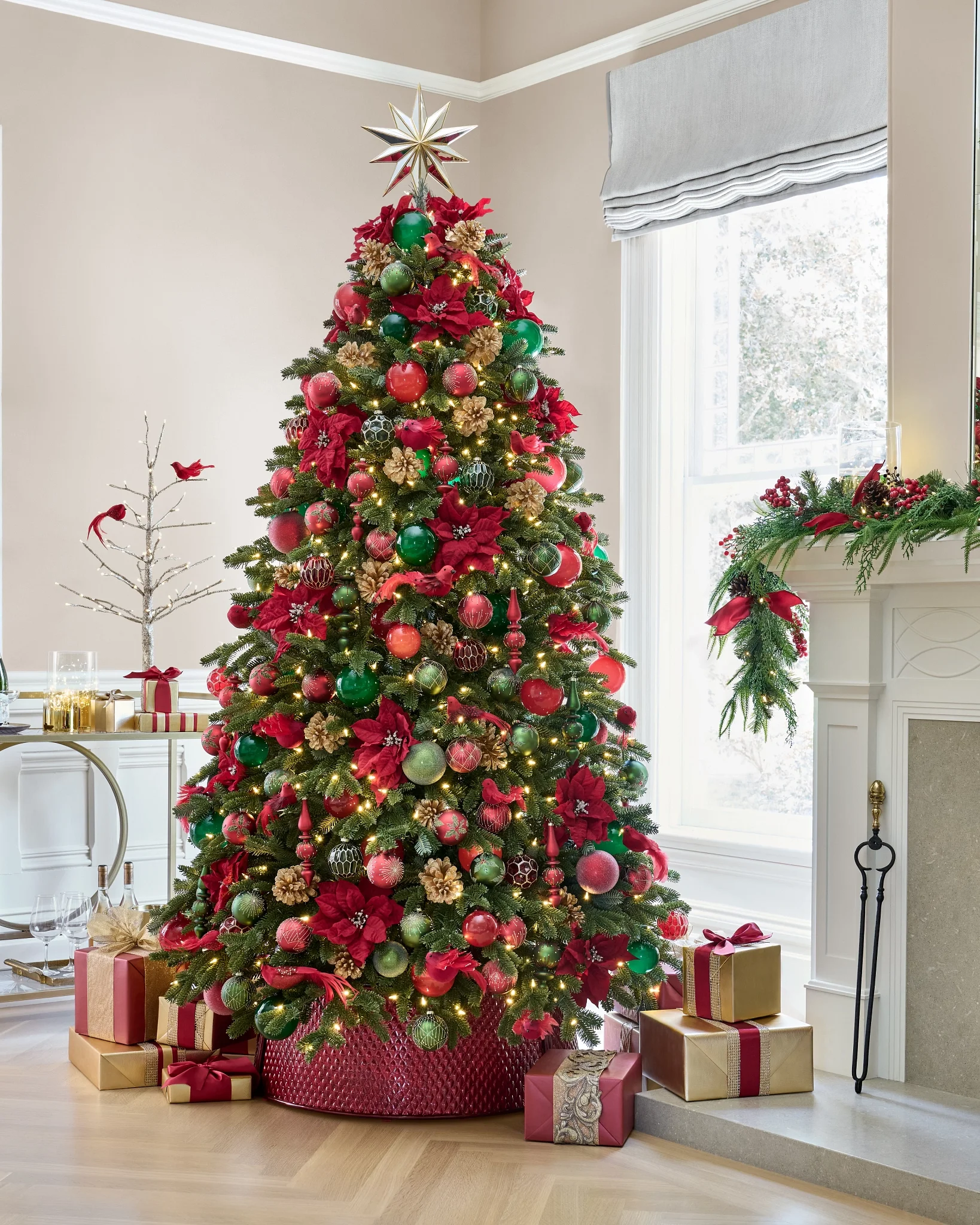 Decorated Christmas tree with red, green, and gold ornaments, surrounded by wrapped gifts, in a well-lit living room with a window and fireplace.