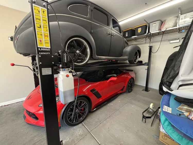 Four post lift with a car stored above a Corvette