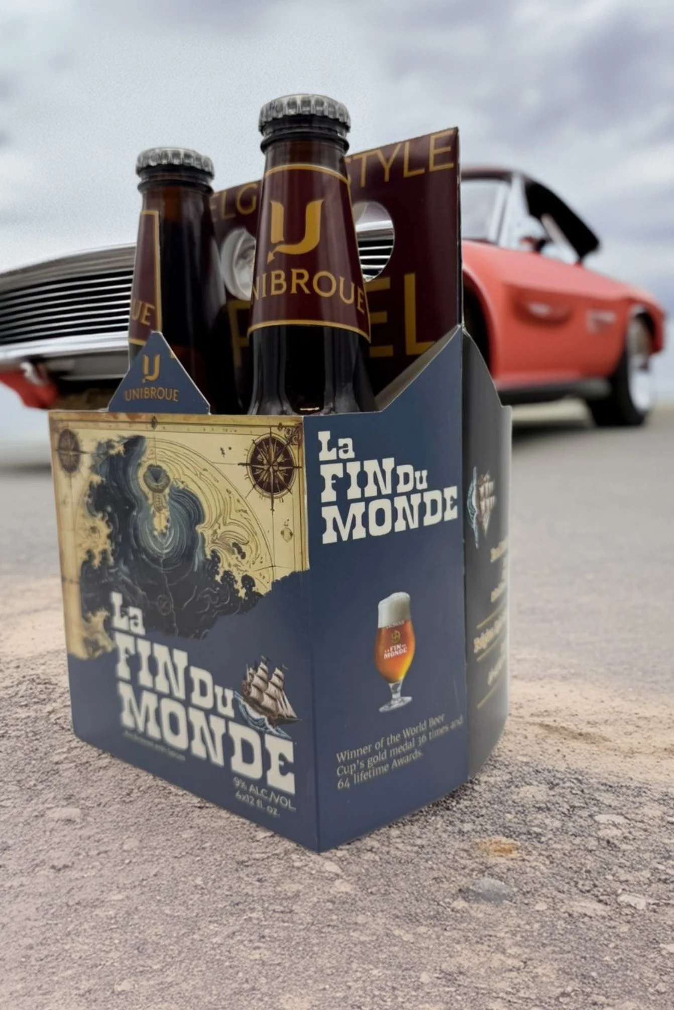 A four pack of beer sitting in front of a classic car