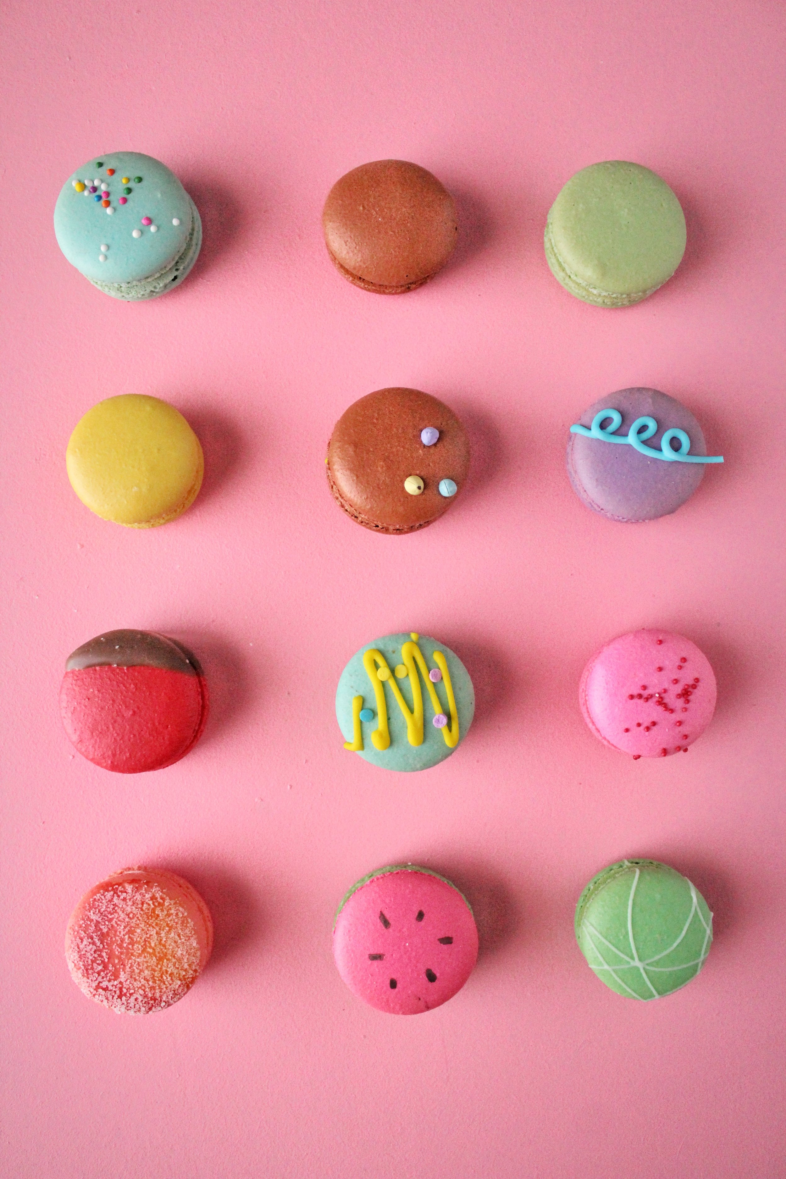 Colorful macarons arranged on a pink surface with various decorations and sprinkles.