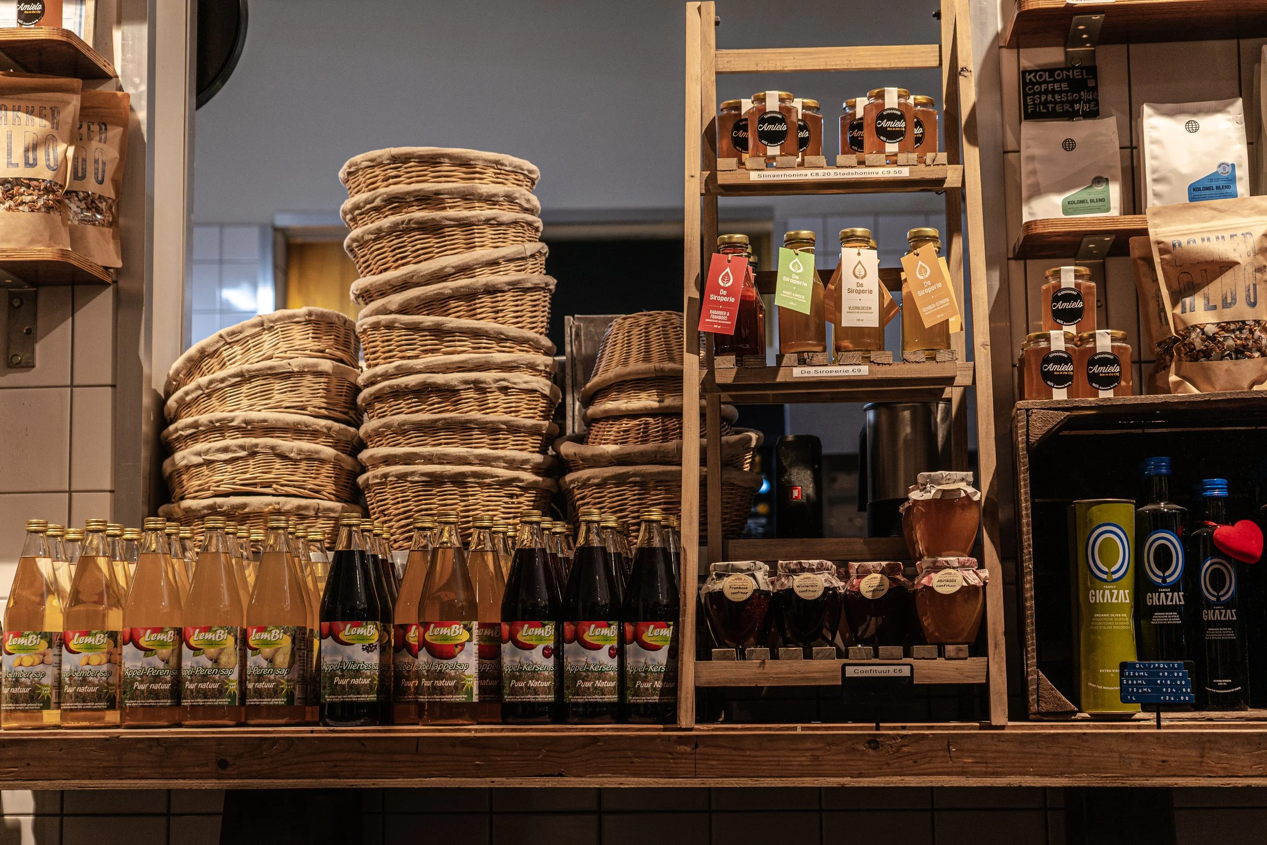 Display of bottled and jarred food products, including apple syrup, in a market or shop setting with baskets and packaging on shelves.