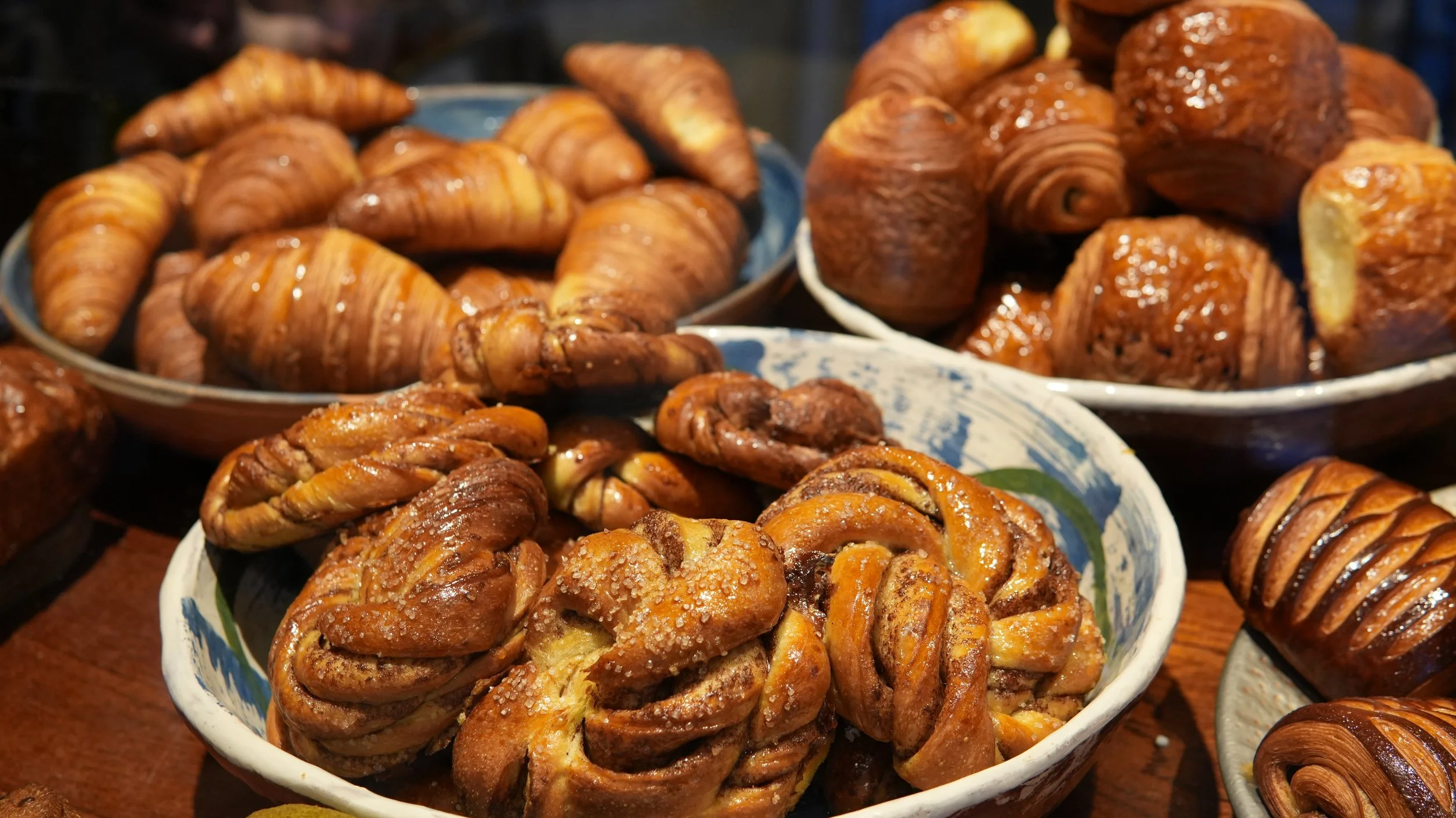 Assorted freshly baked pastries, including croissants, Danish pastries, and rolls, displayed on plates and bowls.