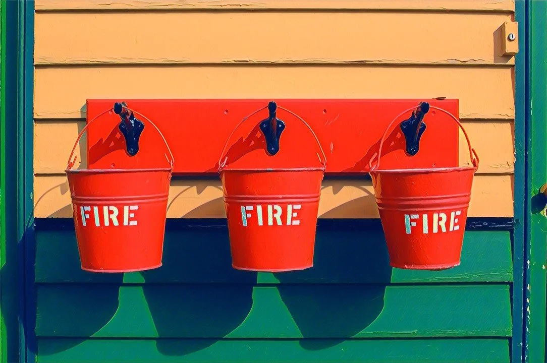 Three red fire buckets hanging on the colorful exterior wall of a house, symbolizing preparedness, balance, and managing financial risk through diversification.