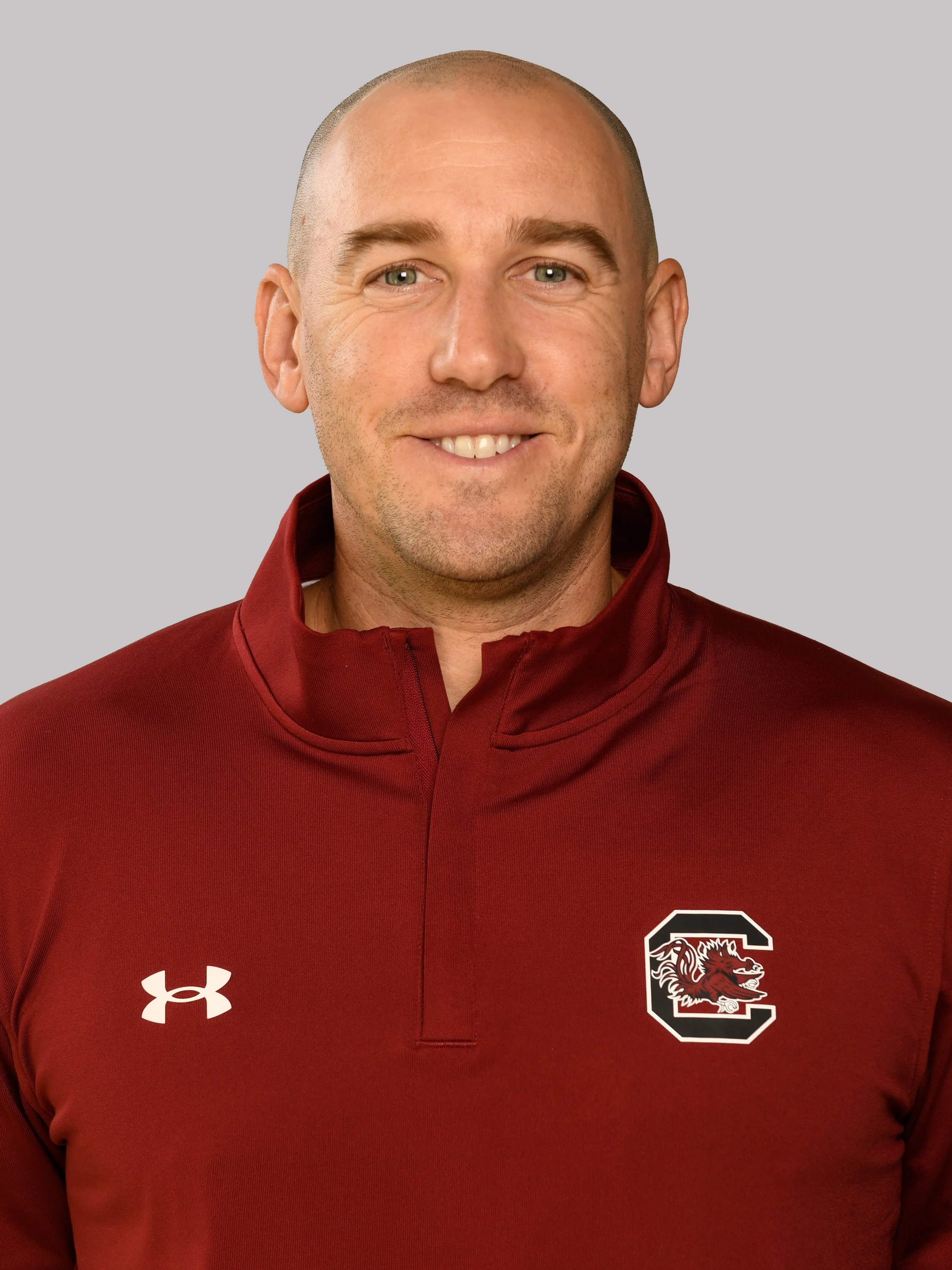 Close-up of a smiling man with short hair wearing a maroon sports jacket with South Carolina Gamecocks logos.