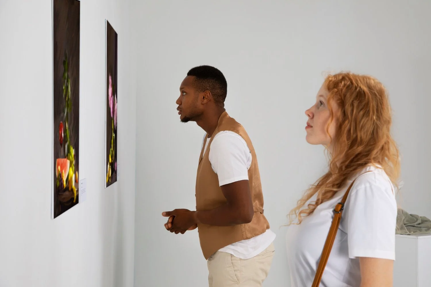 Two people viewing colorful flower photographs on a gallery wall.