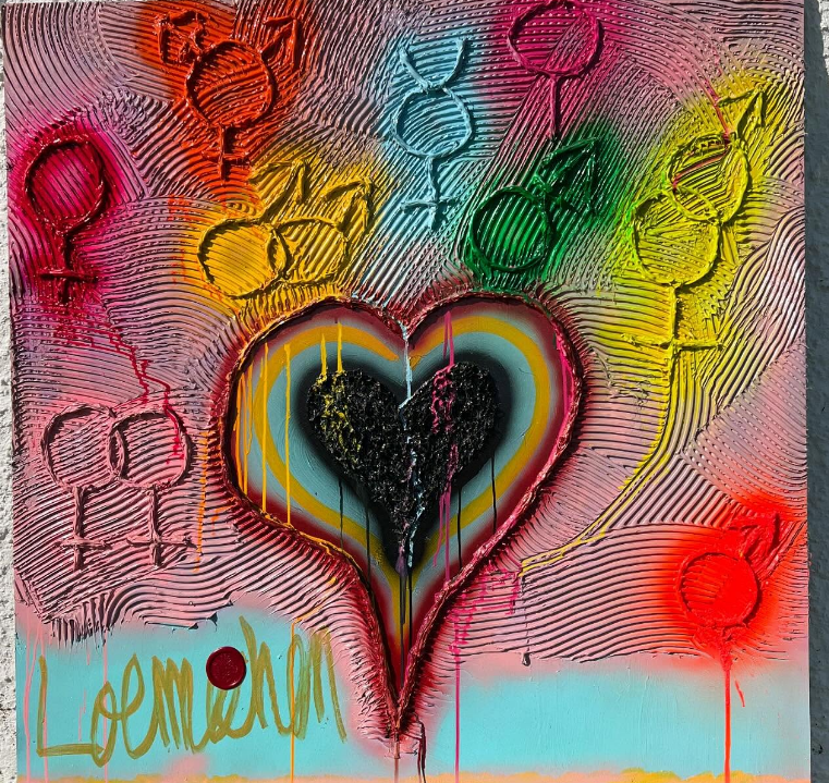 A colorful spray-painted mural featuring a large black heart in the center, surrounded by rainbow-colored concentric circles. Above the heart, there are multiple gender symbols in various colors. The background has textured, swirling lines, and the word "Love" is written at the bottom in gold with a red dot over the "i".