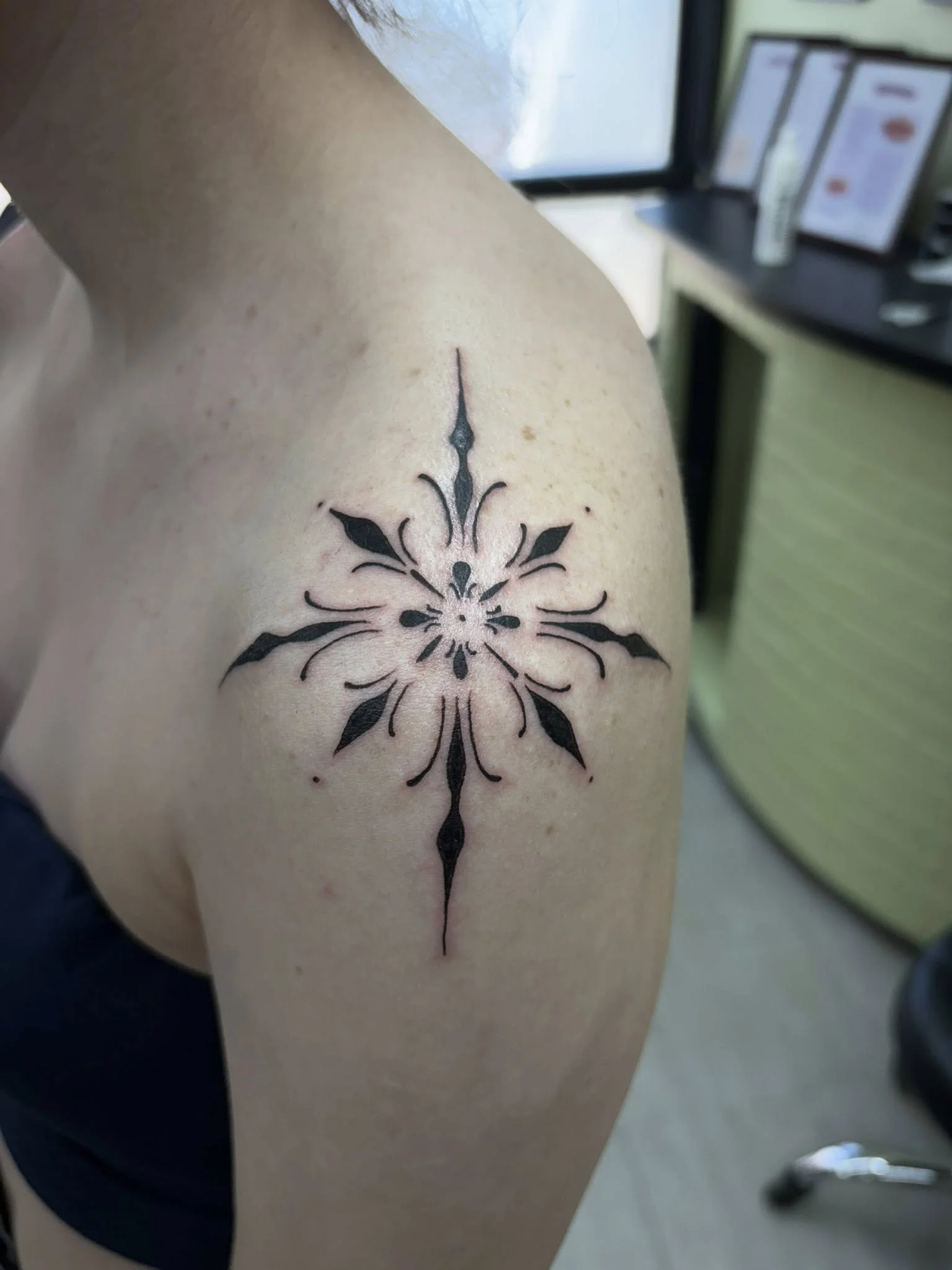 Black geometric tattoo on person's upper arm featuring symmetrical patterns and pointed shapes.