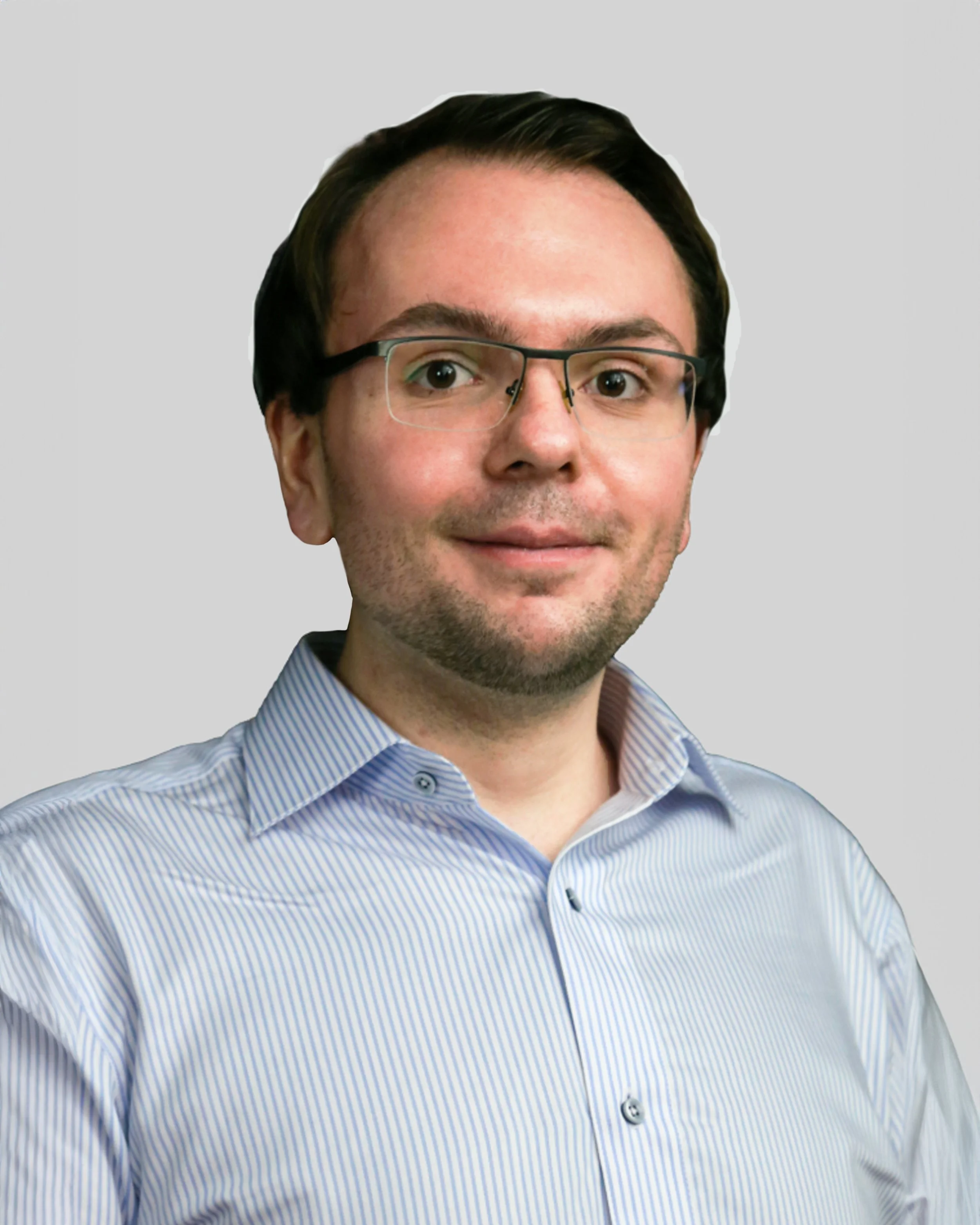 A man with glasses, short dark hair, and a light beard wearing a blue and white striped dress shirt, posing against a plain light gray background.