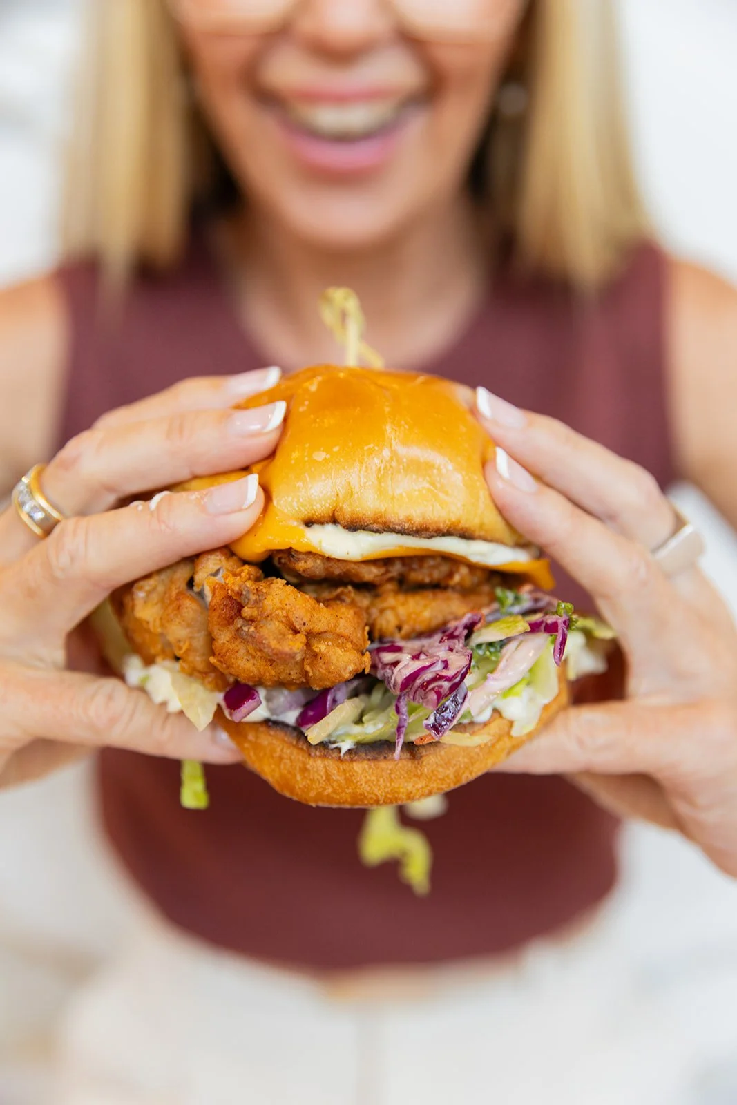 Woman holding a large fried chicken sandwich with cheddar cheese, lettuce, and pickles.
