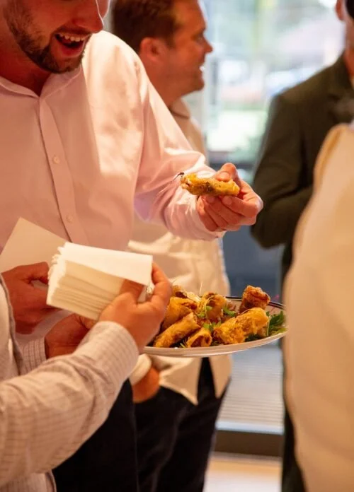People socializing and sharing food at a gathering, with one person holding a plate of chicken wings and another person handing out napkins.