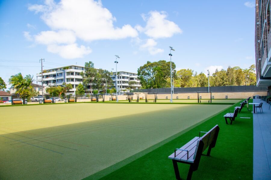 Empty outdoor sports court with benches, surrounded by residential buildings and trees on a sunny day.