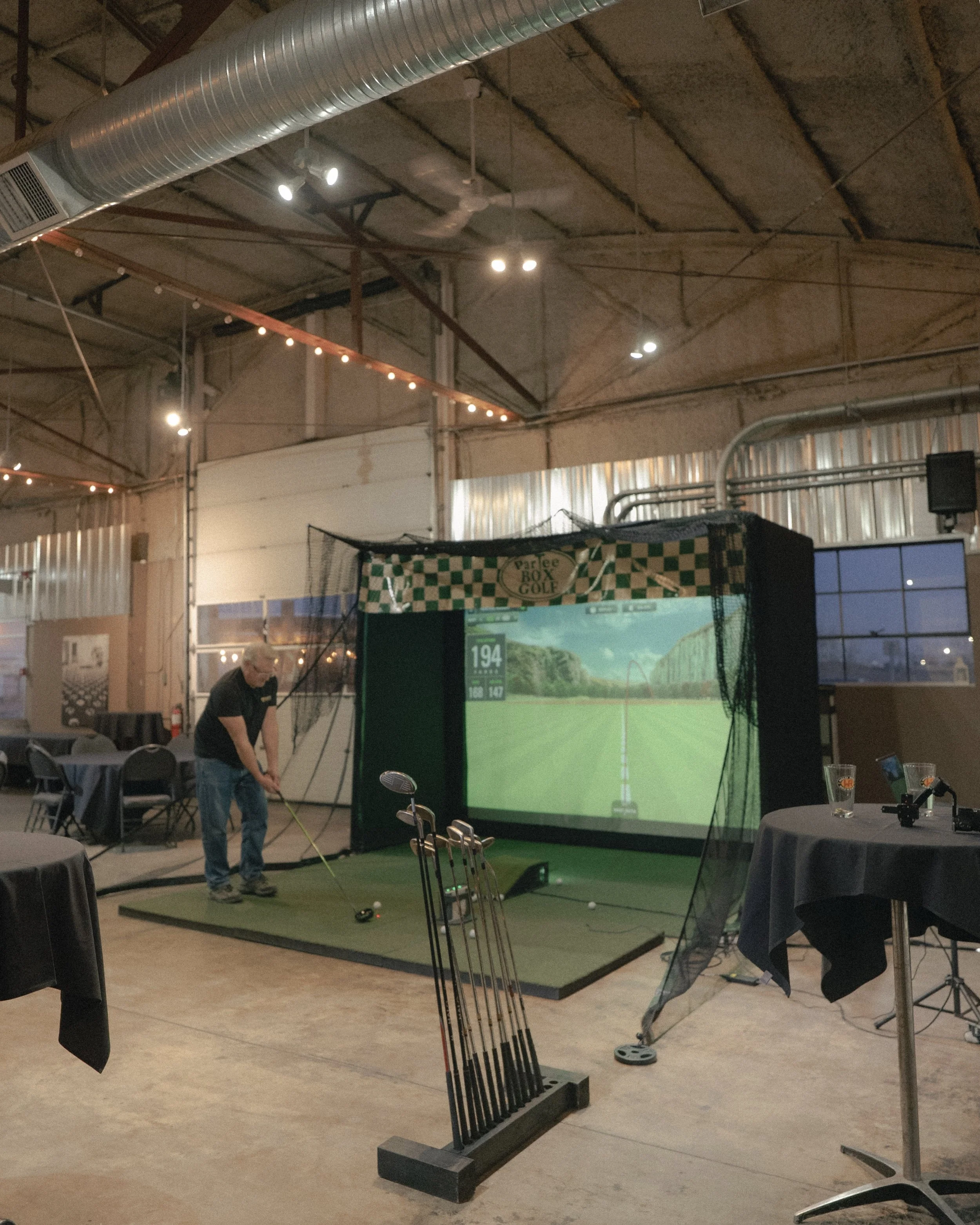 Indoor golf simulation setup with a large screen, golf clubs, and a person practicing their swing.