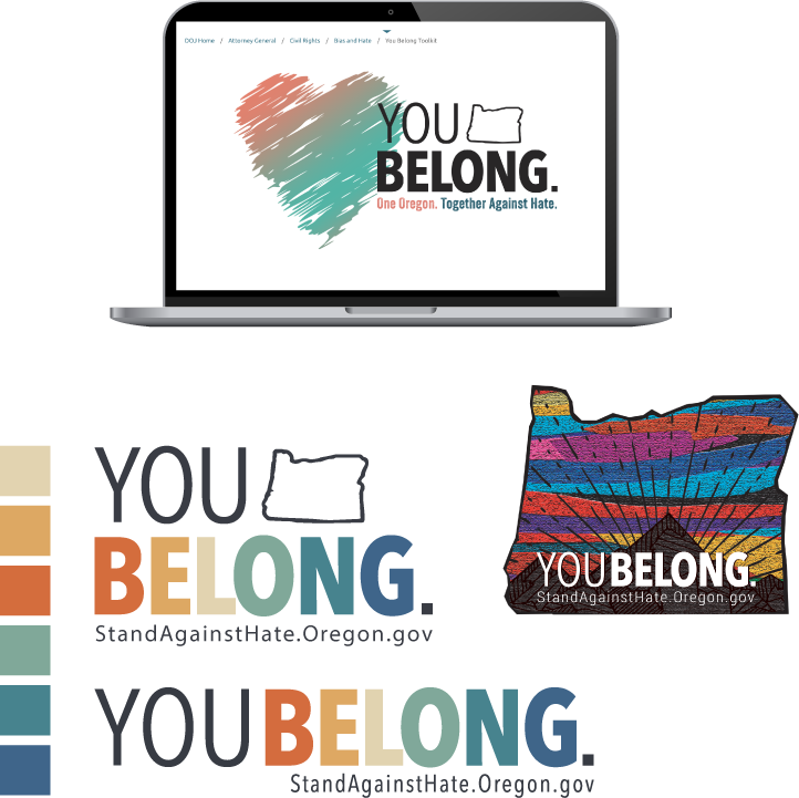 Computer monitor displaying a message from the Oregon Justice Department promoting unity with the slogan "You Belong," featuring a stylized map of Oregon. A table beside it holds various colorful items, and a fabric with rainbow colors and the message "You Belong" is visible.