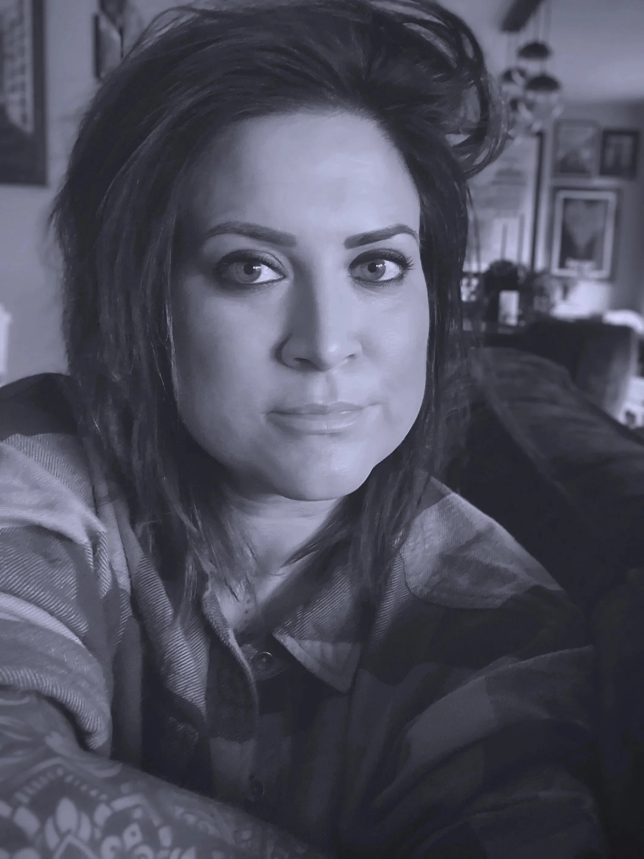 A woman with dark hair and light eyes posing for a selfie in a room with framed artwork on the wall.