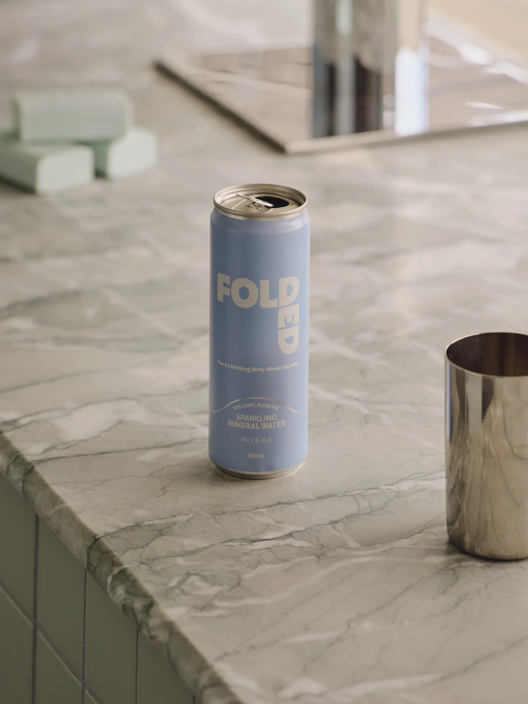 A can of FOURED sparkling mineral water on a marble countertop, with a silver cup next to it.