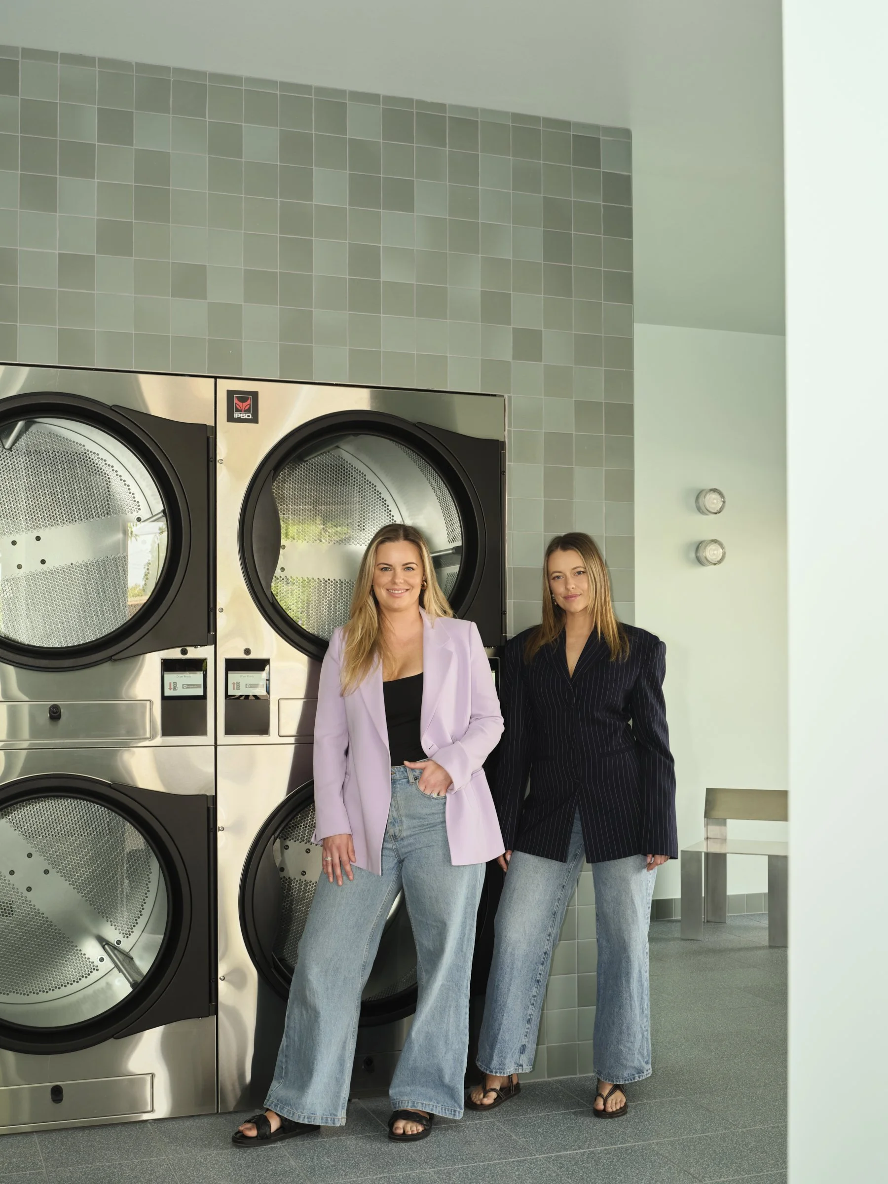 Founders of Folded Laundromat standing in front of a stack of large commercial self-service washers in laundromat.