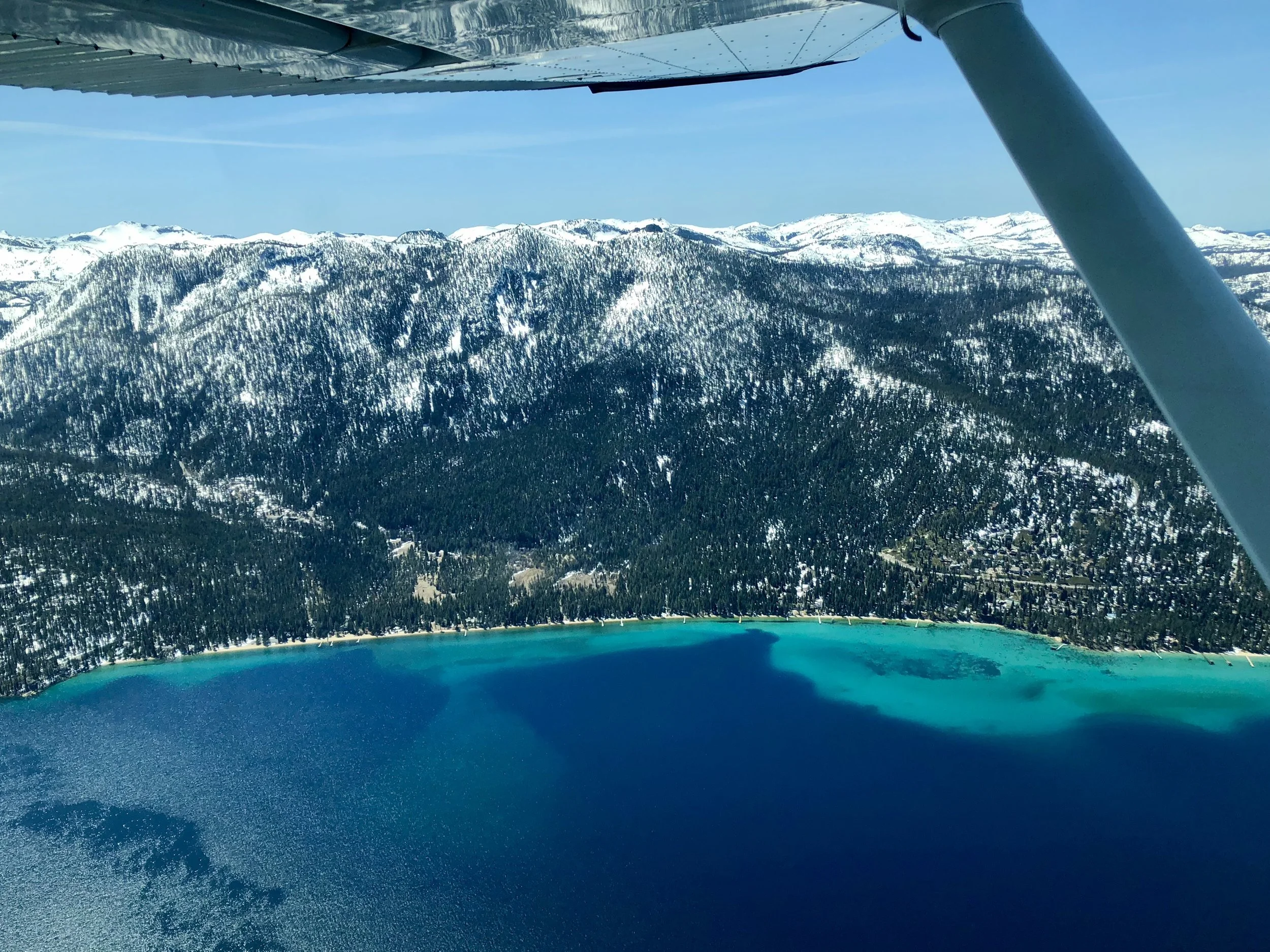 Lake Tahoe with snowy mountains and emerald green water as seen from an airplane. North Tahoe Aviation air tour, sight seeing tour. 
