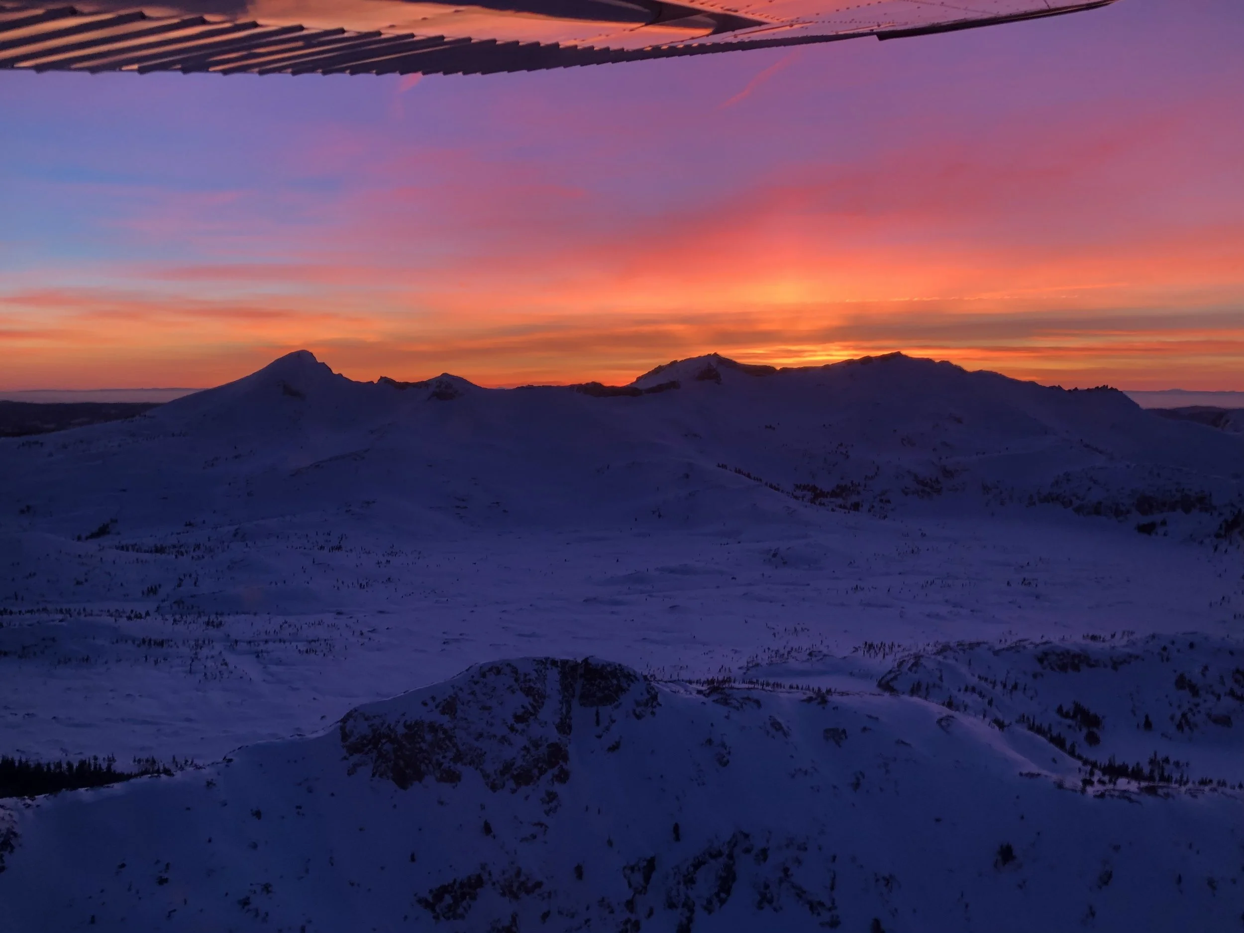 Snow-covered mountain range at sunset with a colorful sky of pink, purple, and orange hues.