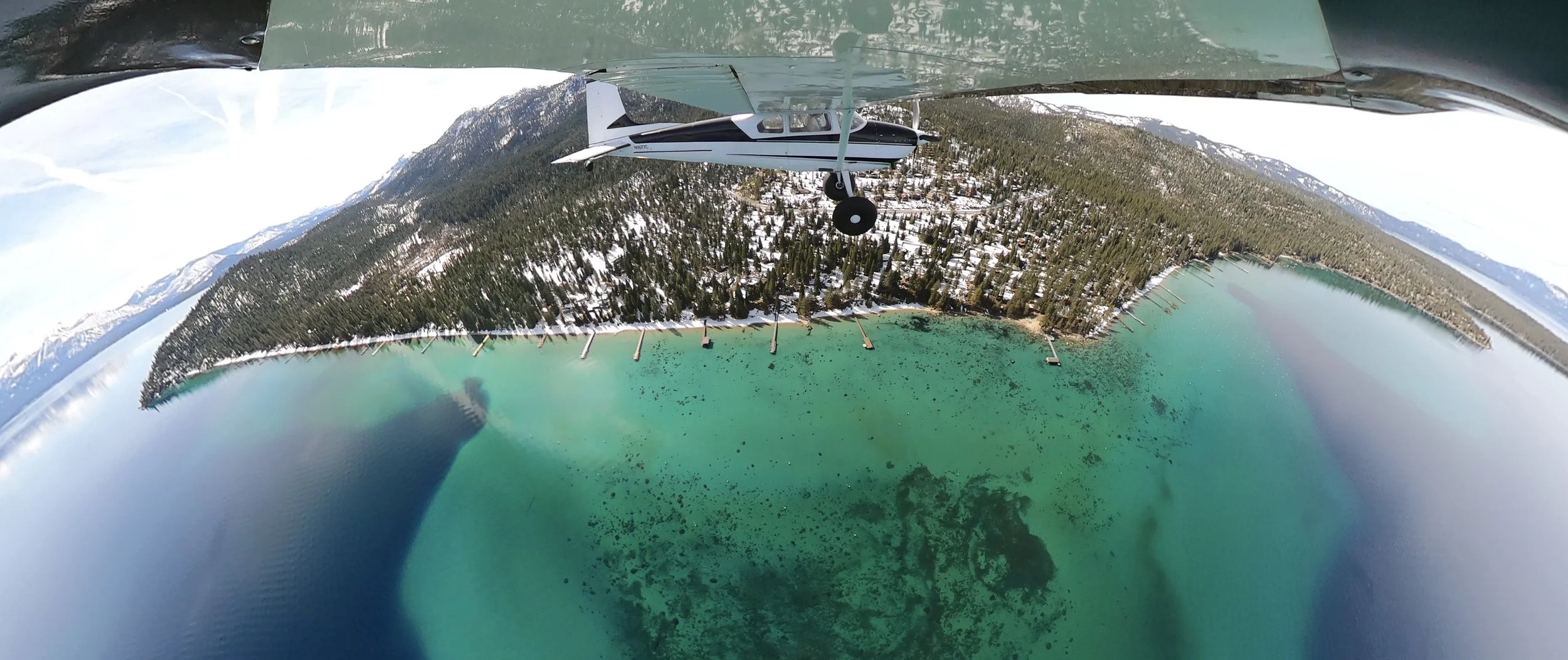 North Tahoe Aviations Cessna 180 flying over the emerald water of Lake Tahoe on a sightseeing tour.