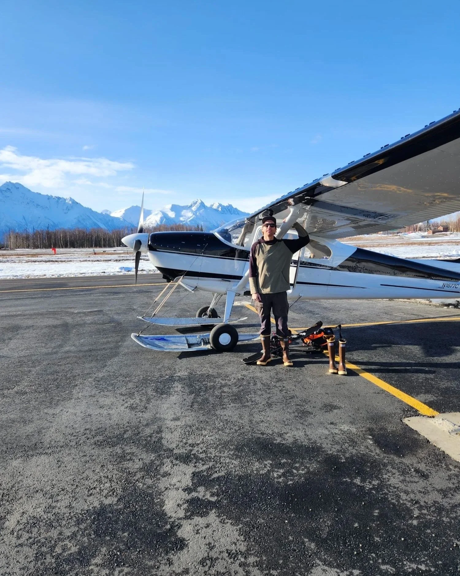 Keith Davis, next to his 1953 Cessna 180 ski plane, with snow-covered mountains and a clear blue sky.