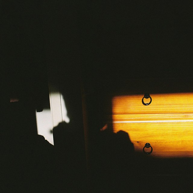 Sunlight shining through blinds creating shadows on a wall and wooden surface.
