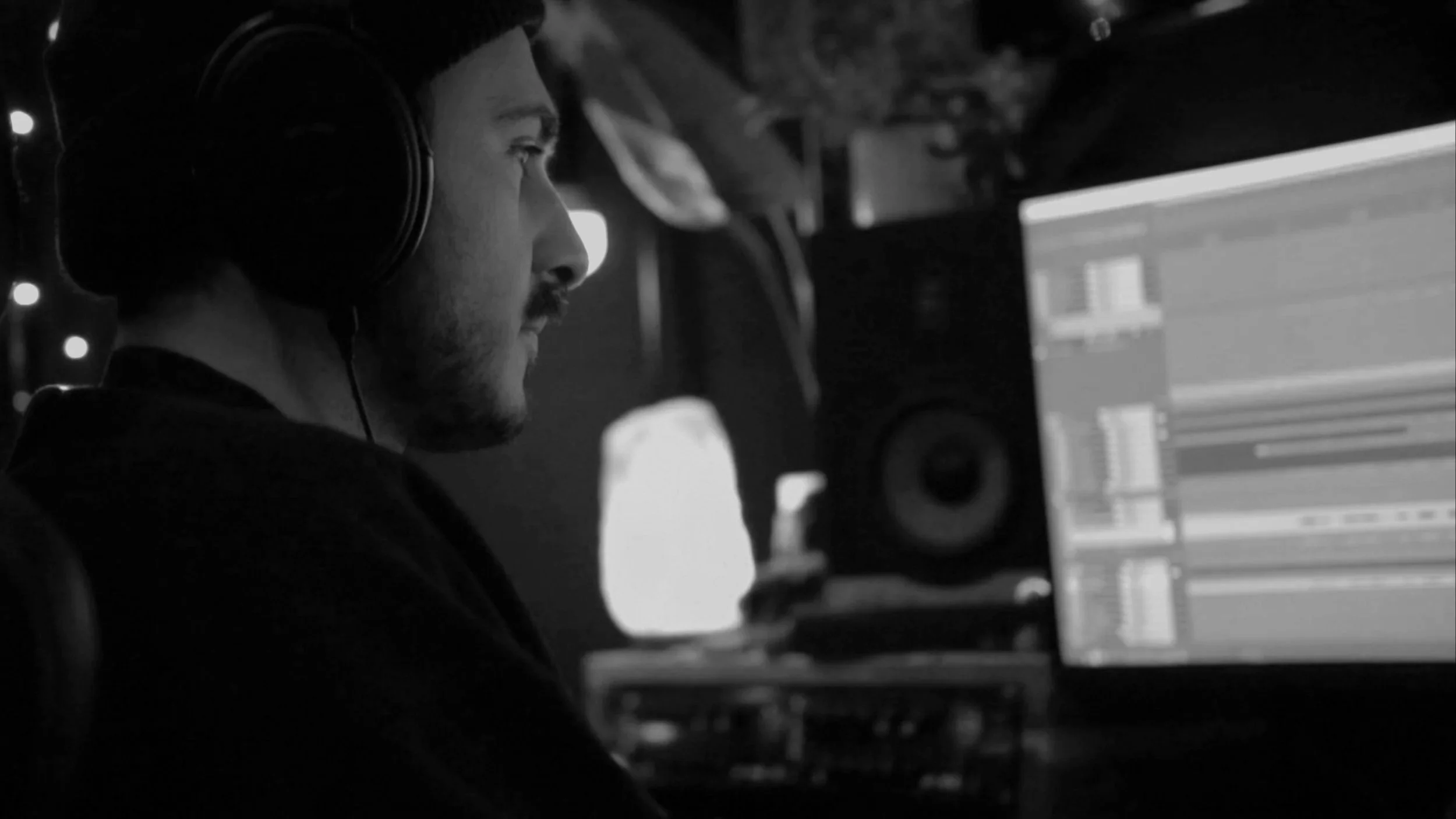A person with headphones working on a computer in a dimly lit room.