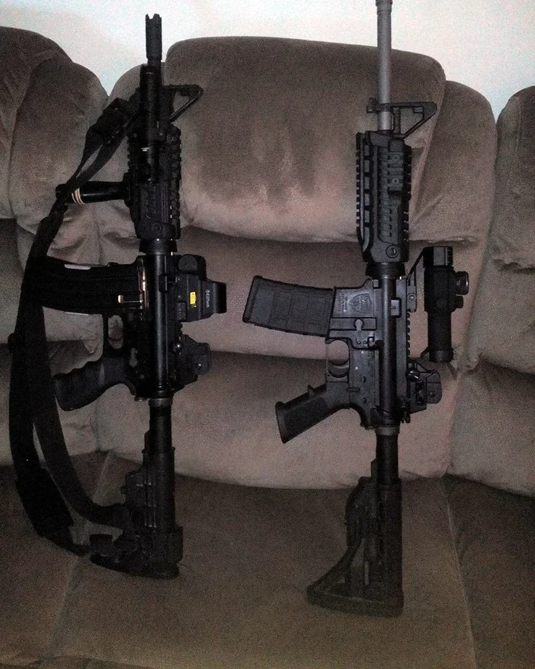 Two black tactical rifles leaning against a beige couch.