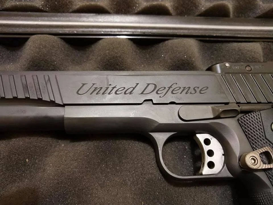 A handgun with the words "United Defense" engraved on the slide, placed on a foam-lined case.