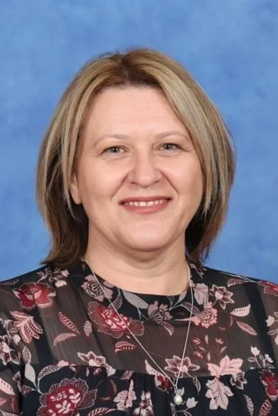 A woman with shoulder-length blonde hair and a floral patterned top poses against a blue background.
