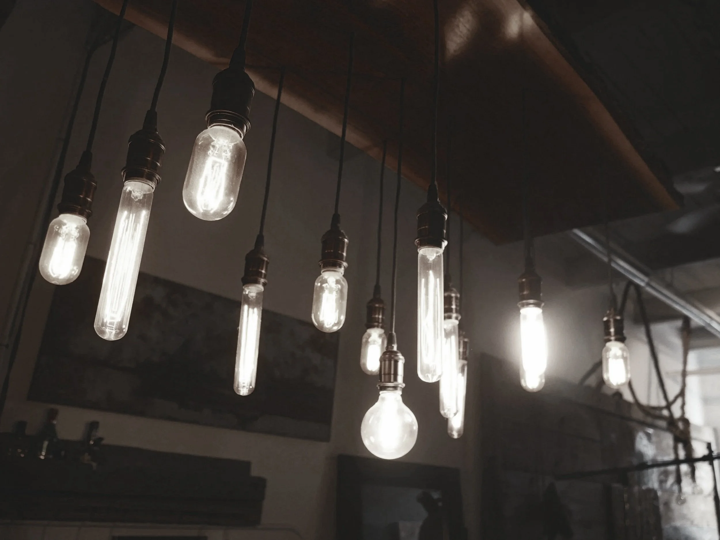 Several hanging Edison-style light bulbs with exposed filaments turned on, suspended from a dark ceiling in a dimly lit room.