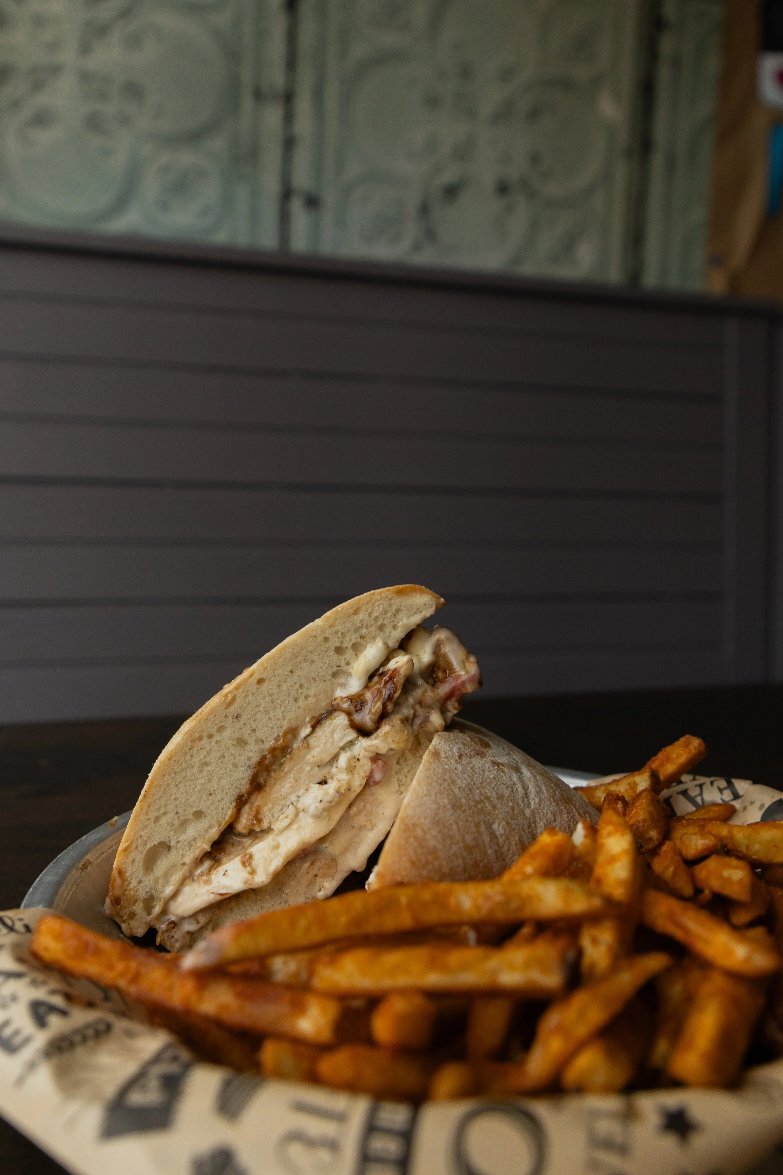Behind a bed of fries, a chicken sandwich rest on its other half. In it burrata and red roasted peppers.