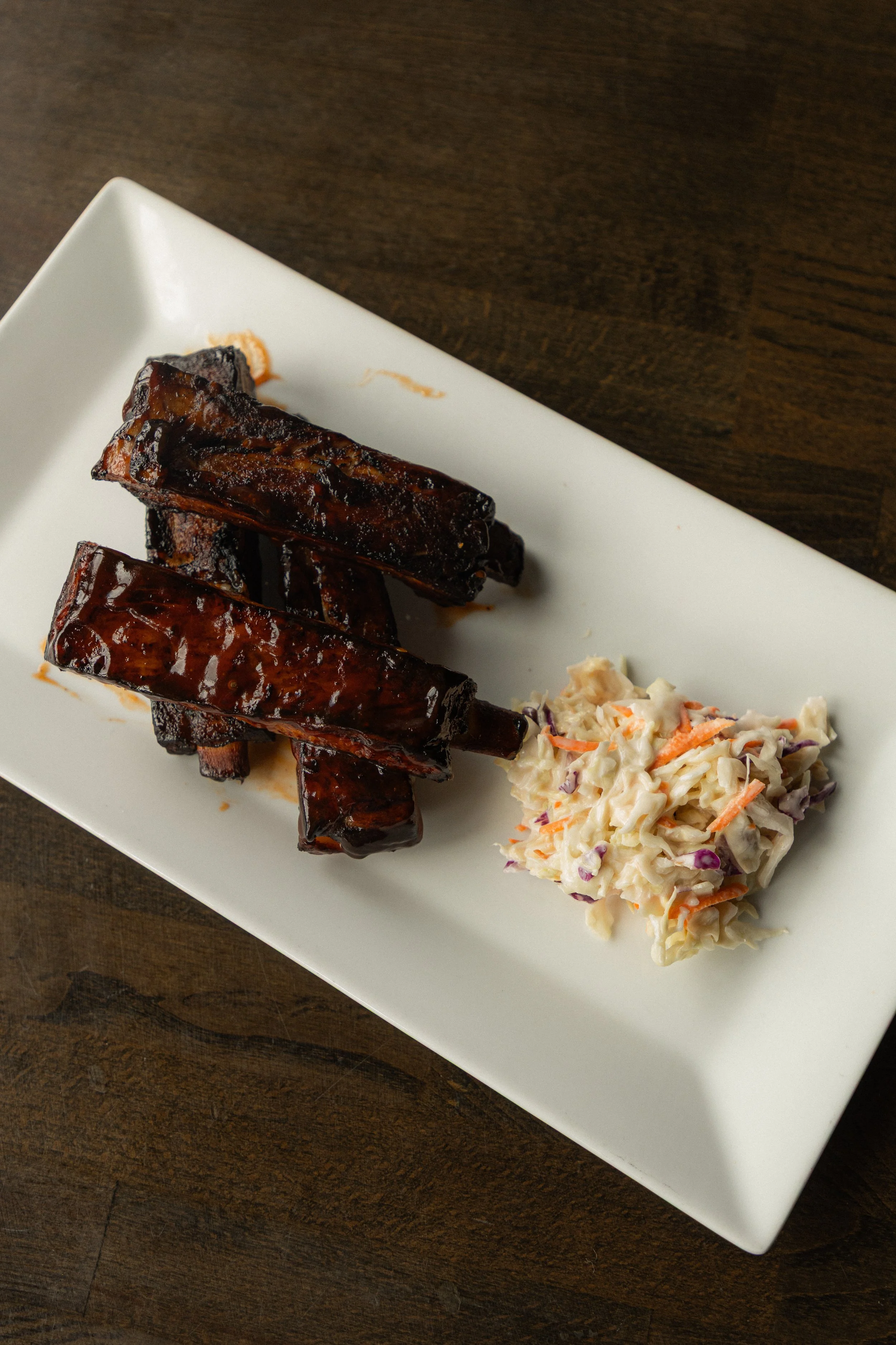 Overhead shot of 4 BBQ ribs stacked on top of eachother with a spoonful of coleslaw on the side.
