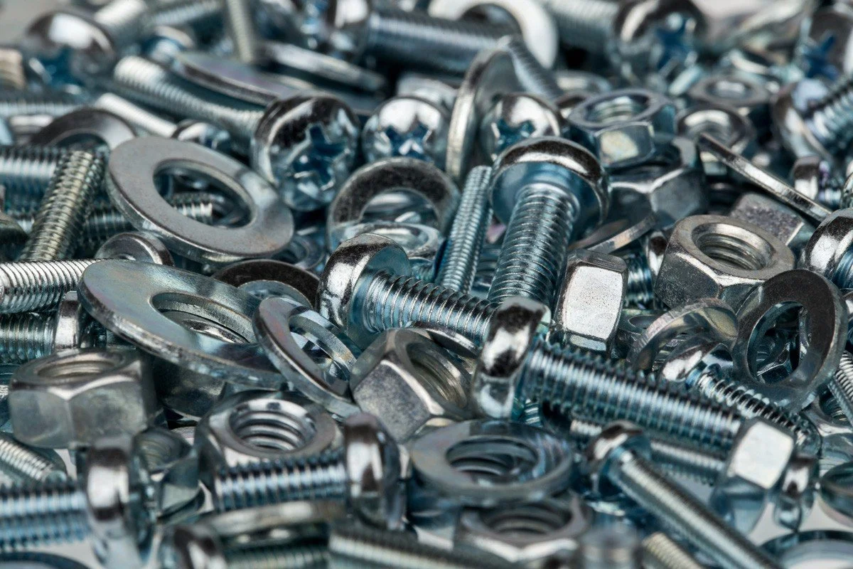 A pile of shiny metallic bolts, nuts, and washers scattered together.