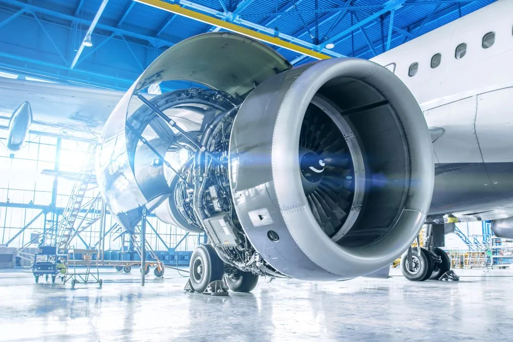 Close-up of a commercial airplane engine at an aircraft manufacturing facility with stairs and equipment in the background.