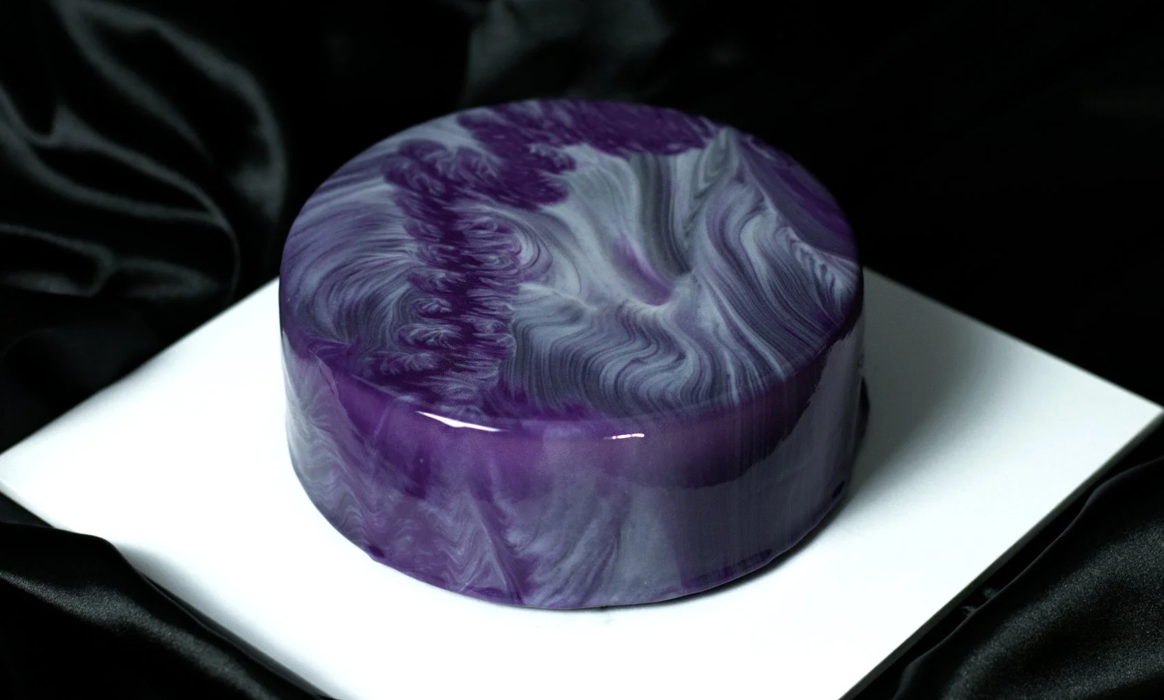 Luxury round entremet dessert by AFTERSIX with purple and grey marble mirror glaze, displayed on a white platform against a dark backdrop, tagged with the name 'SLIQ'.