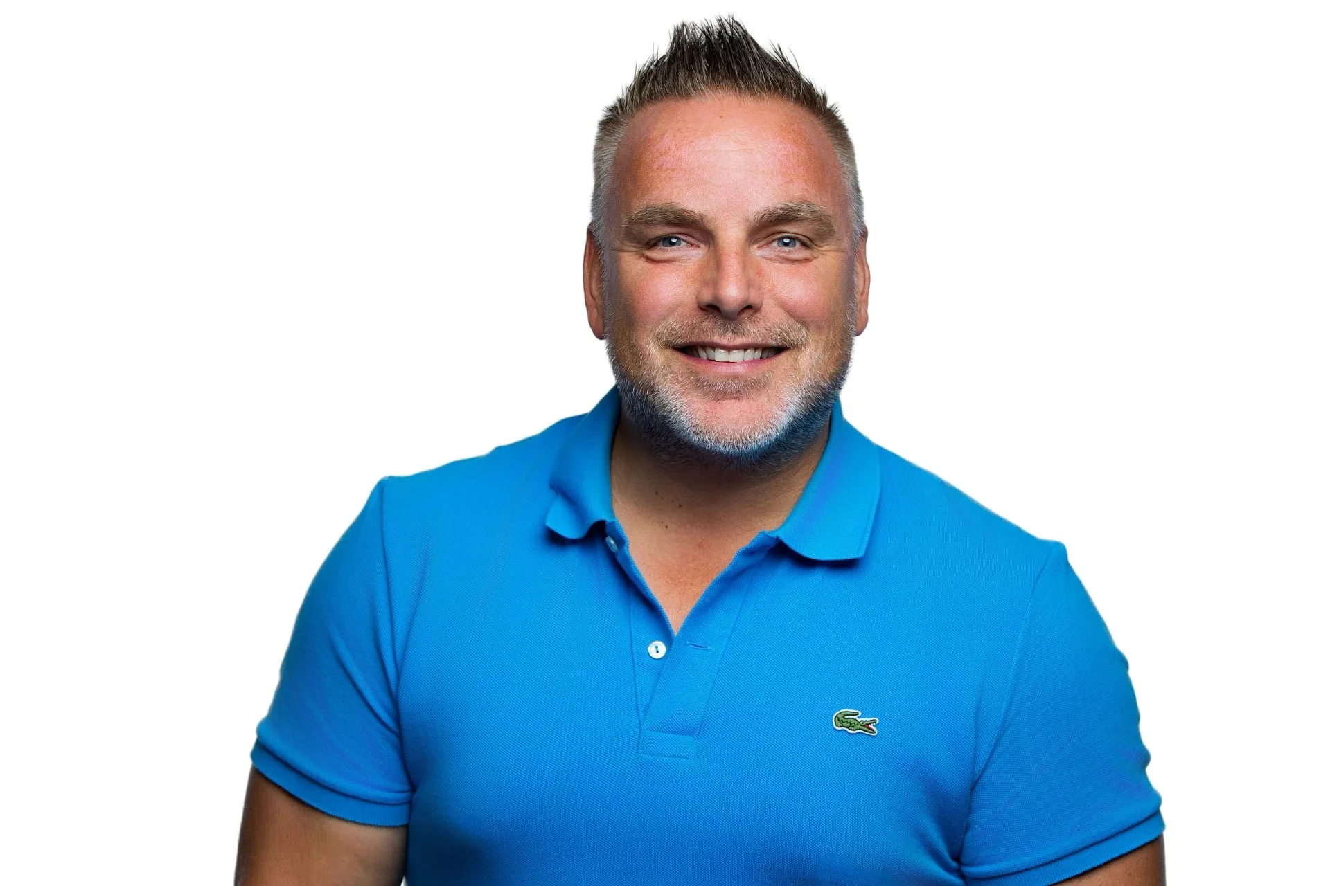 Portrait of a smiling man with short gray hair, wearing a blue polo shirt with Lacoste crocodile logo, against a white background.