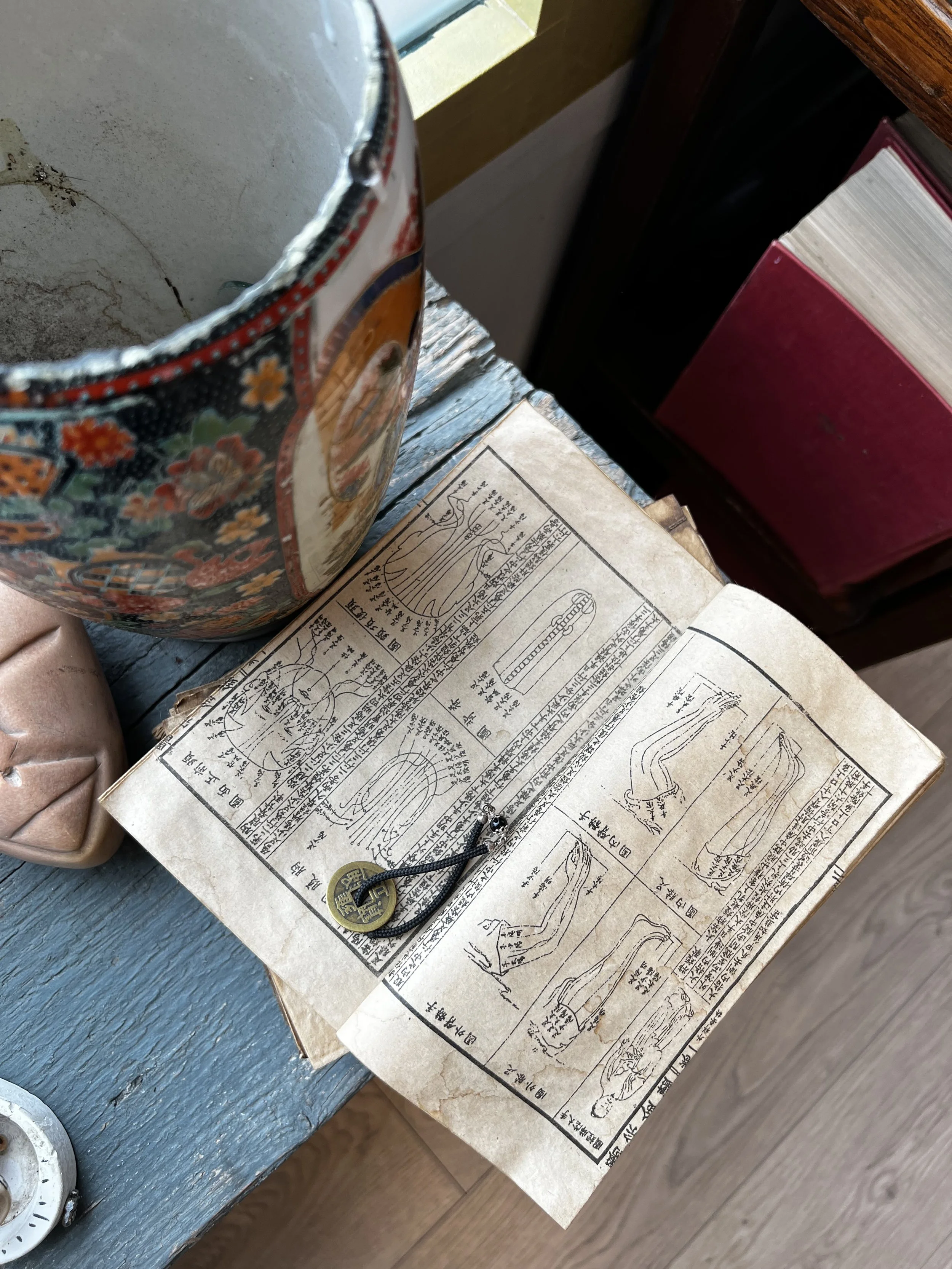 Un libro aperto con illustrazioni e testo in cinese, accanto a un oggetto circolare con un cordino e una moneta, su un tavolo di legno blu.