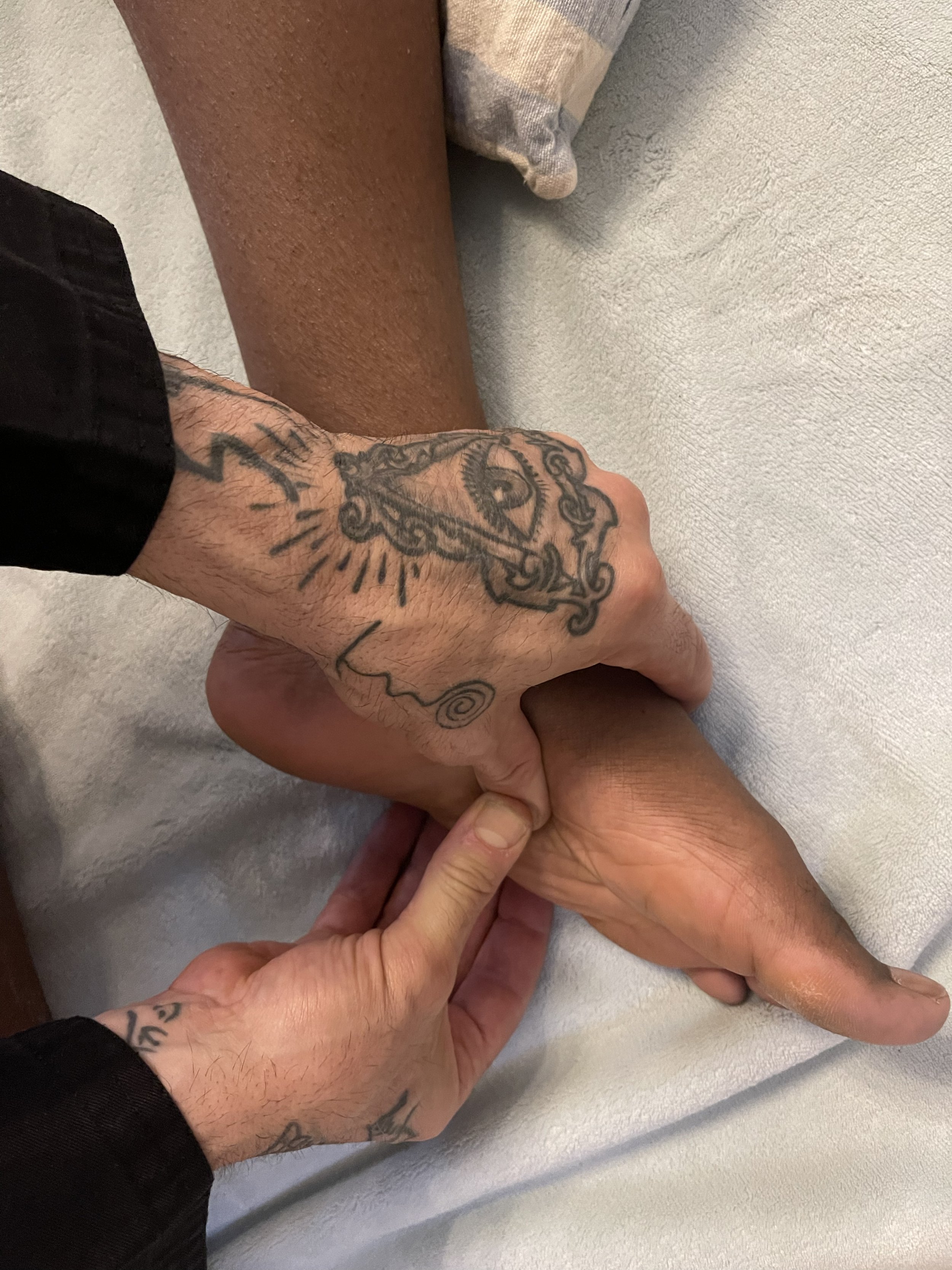 Due mani si tengono stretti, una di fronte ad un letto con una persona sdraiata. La mano visibile ha tatuaggi, tra cui un'occhio e un cuore con una linea che si allunga.