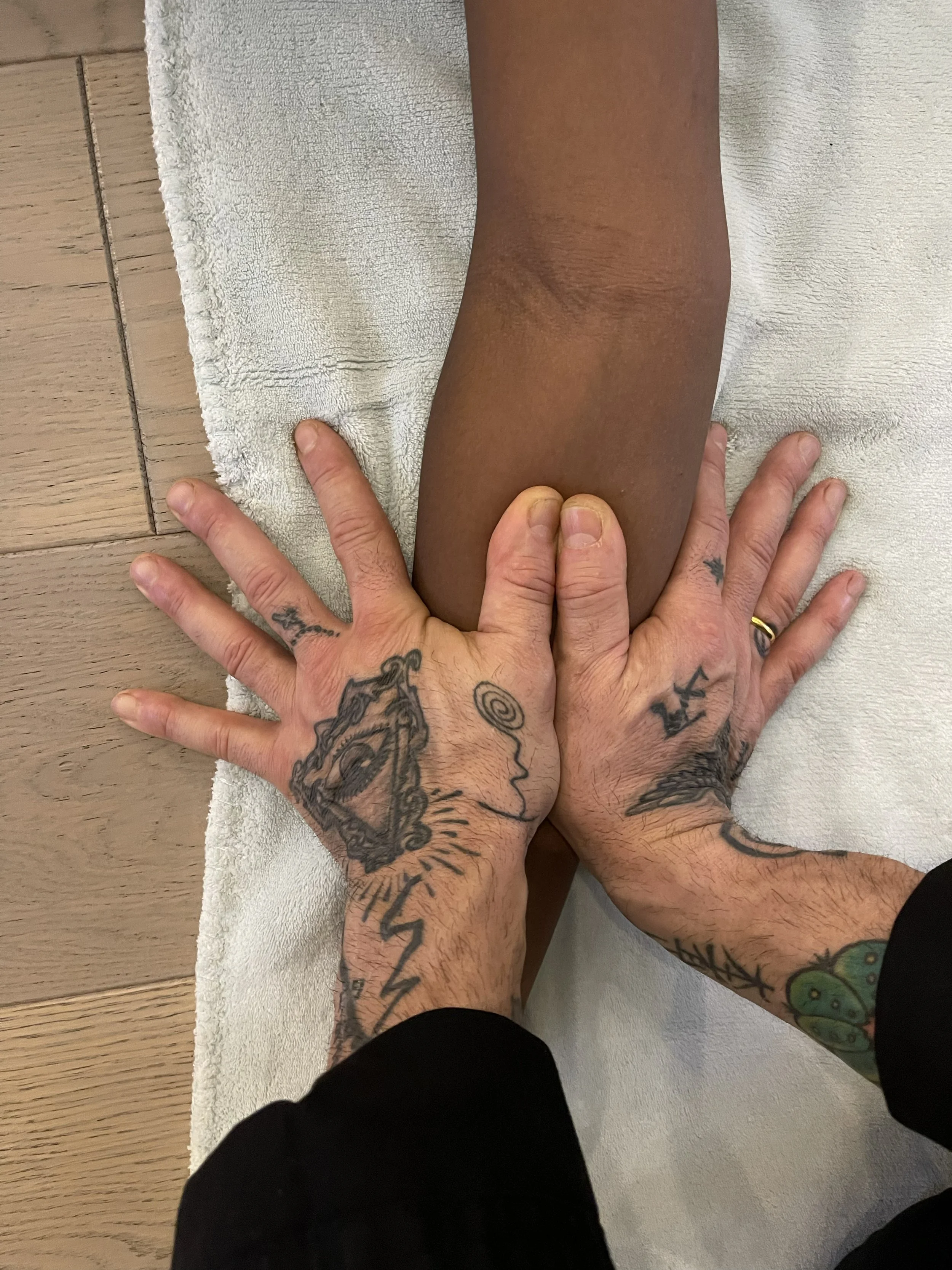Una persona sta facendo terapia o massaggi al braccio di un'altra persona su un tappetino bianco, con un pavimento di legno visibile.