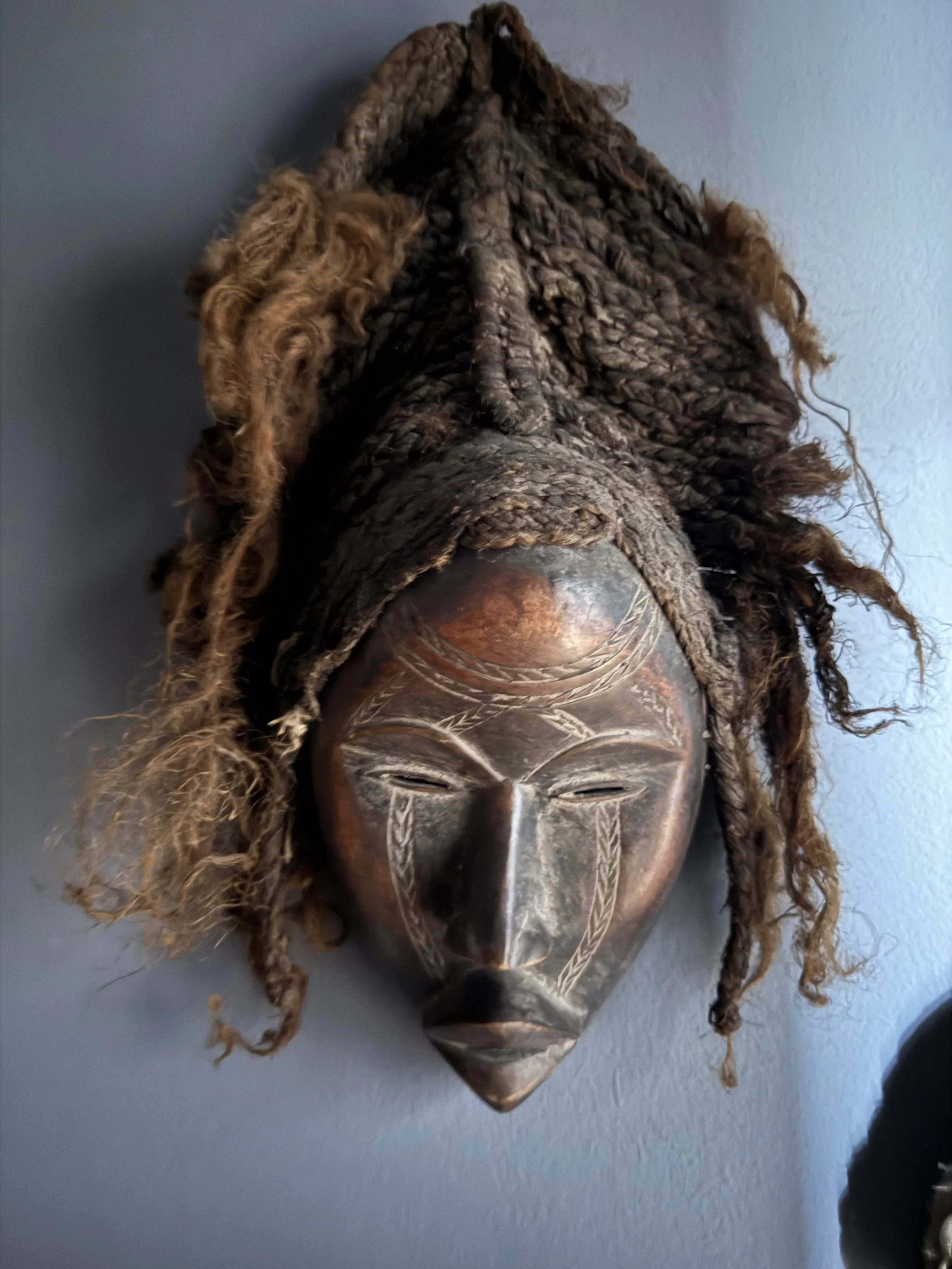 Maschera africana decorativa con elementi in legno e capelli dreads.