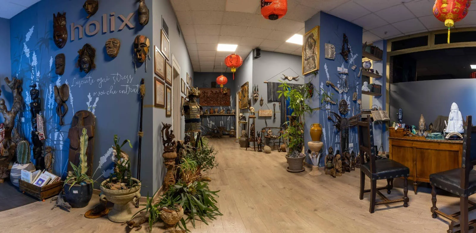 Interno di un negozio di antiquariato decorato con maschere etniche appese al muro, piante in vasi, lampade di carta rosse e vari oggetti artistici e d'antiquariato.