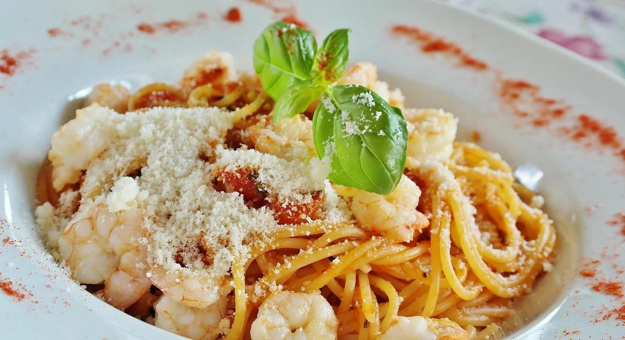 Plate of shrimp pasta garnished with basil leaves and grated cheese, with a sprinkle of paprika around the rim.